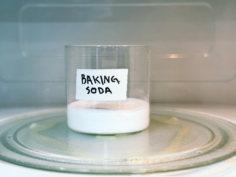 A glass container with baking soda in it inside a microwave oven