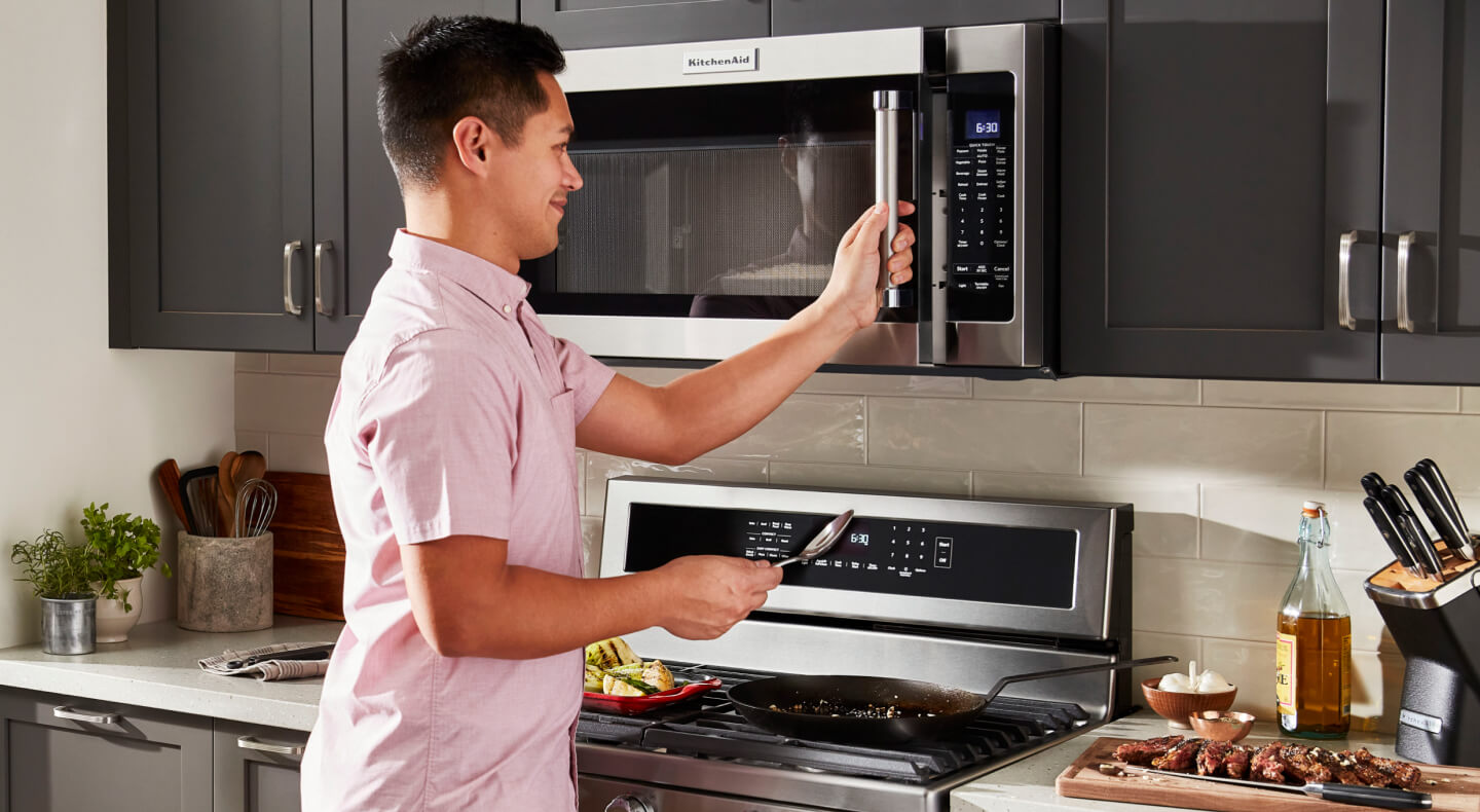 A smiling man opening the door of his microwave oven in his kitchen
