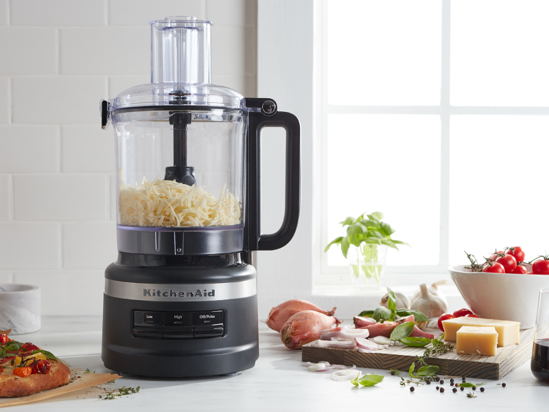 Shredded cheese in a food processor next to a pizza