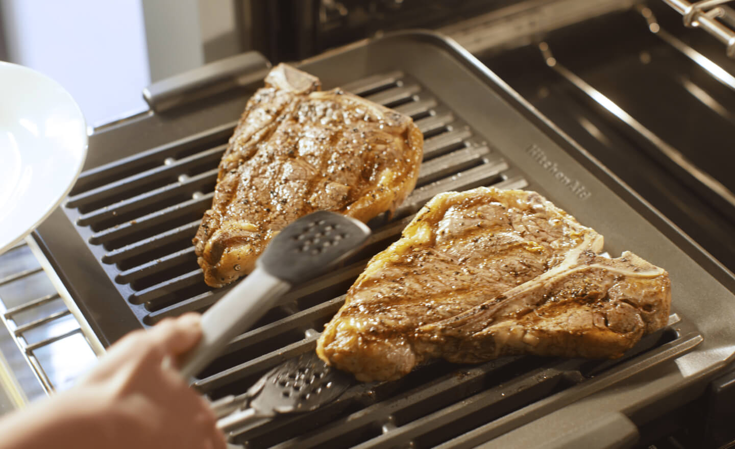 A person grilling meat in a KitchenAid® oven