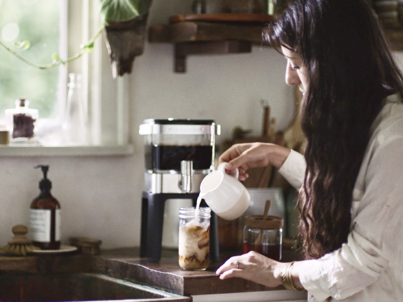 Person pouring milk into cup of cold brew coffee Person pouring milk into cup of cold brew coffee