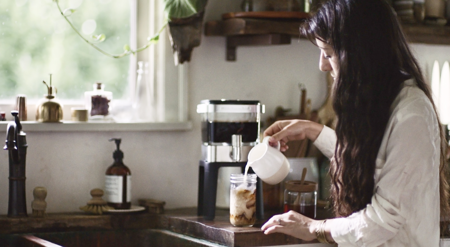 Person pouring milk into cup of cold brew coffee Person pouring milk into cup of cold brew coffee