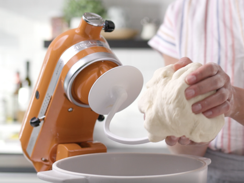 Bread dough being removed from a dough hook attached to an orange tilt-head KitchenAid® stand mixer. Bread dough being removed from a dough hook attached to an orange tilt-head KitchenAid® stand mixer.