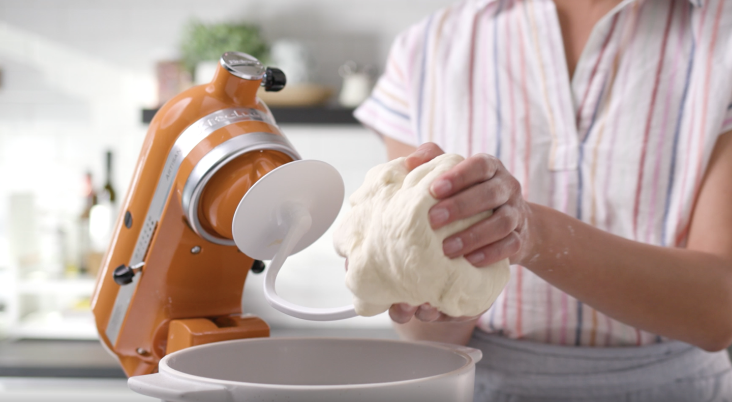 Bread dough being removed from a dough hook attached to an orange tilt-head KitchenAid® stand mixer. Bread dough being removed from a dough hook attached to an orange tilt-head KitchenAid® stand mixer.