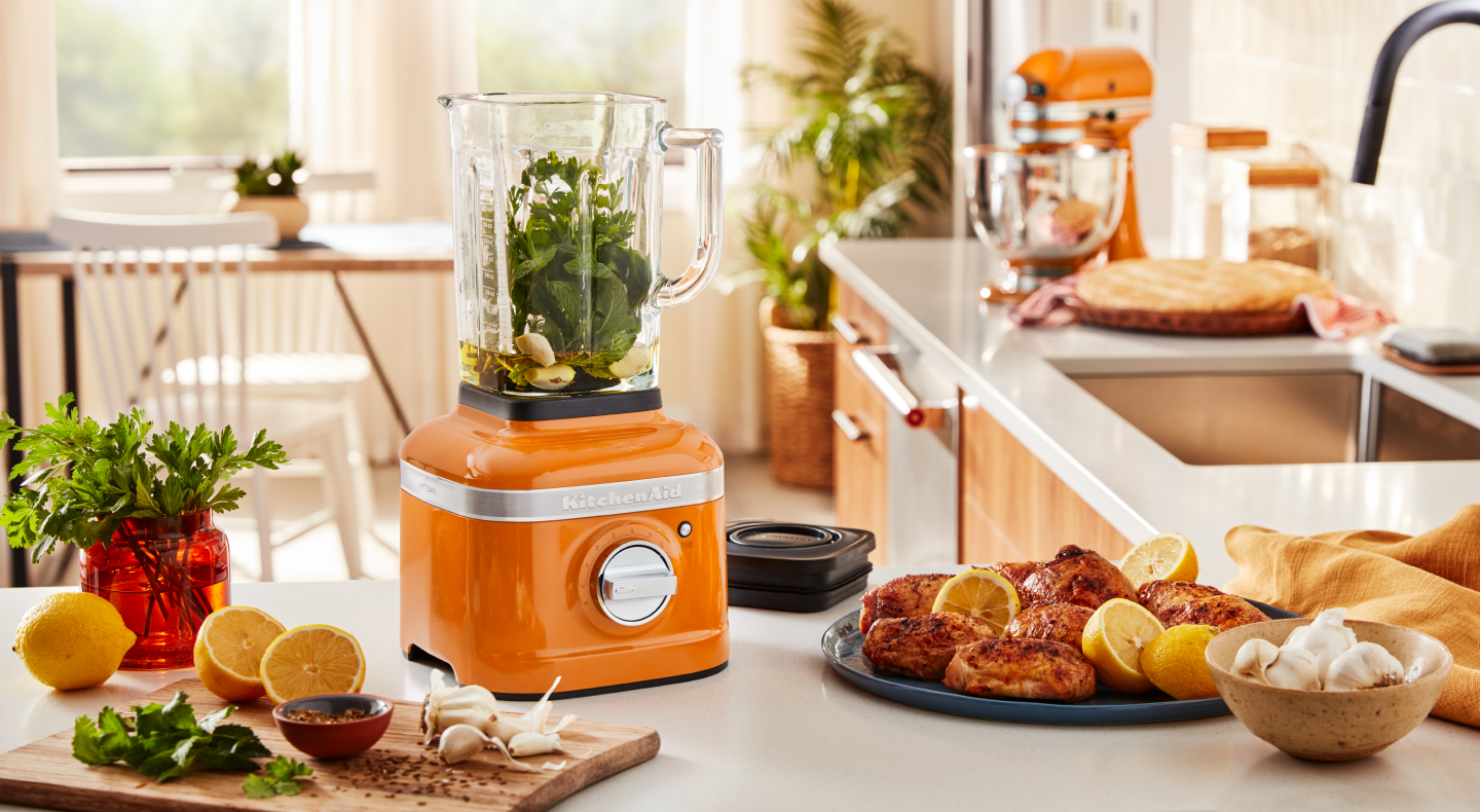 An orange KitchenAid® blender with sliced oranges and grilled chicken nearby. An orange KitchenAid® blender with sliced oranges and grilled chicken nearby.