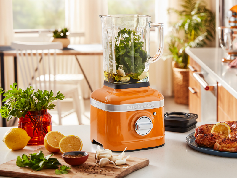 An orange KitchenAid® blender with sliced oranges and grilled chicken nearby. An orange KitchenAid® blender with sliced oranges and grilled chicken nearby.