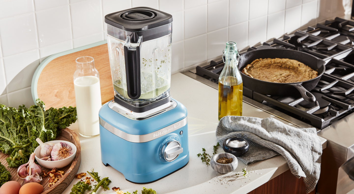 A KitchenAid® blender surrounded by various herbs and vegetable oil. A KitchenAid® blender surrounded by various herbs and vegetable oil.