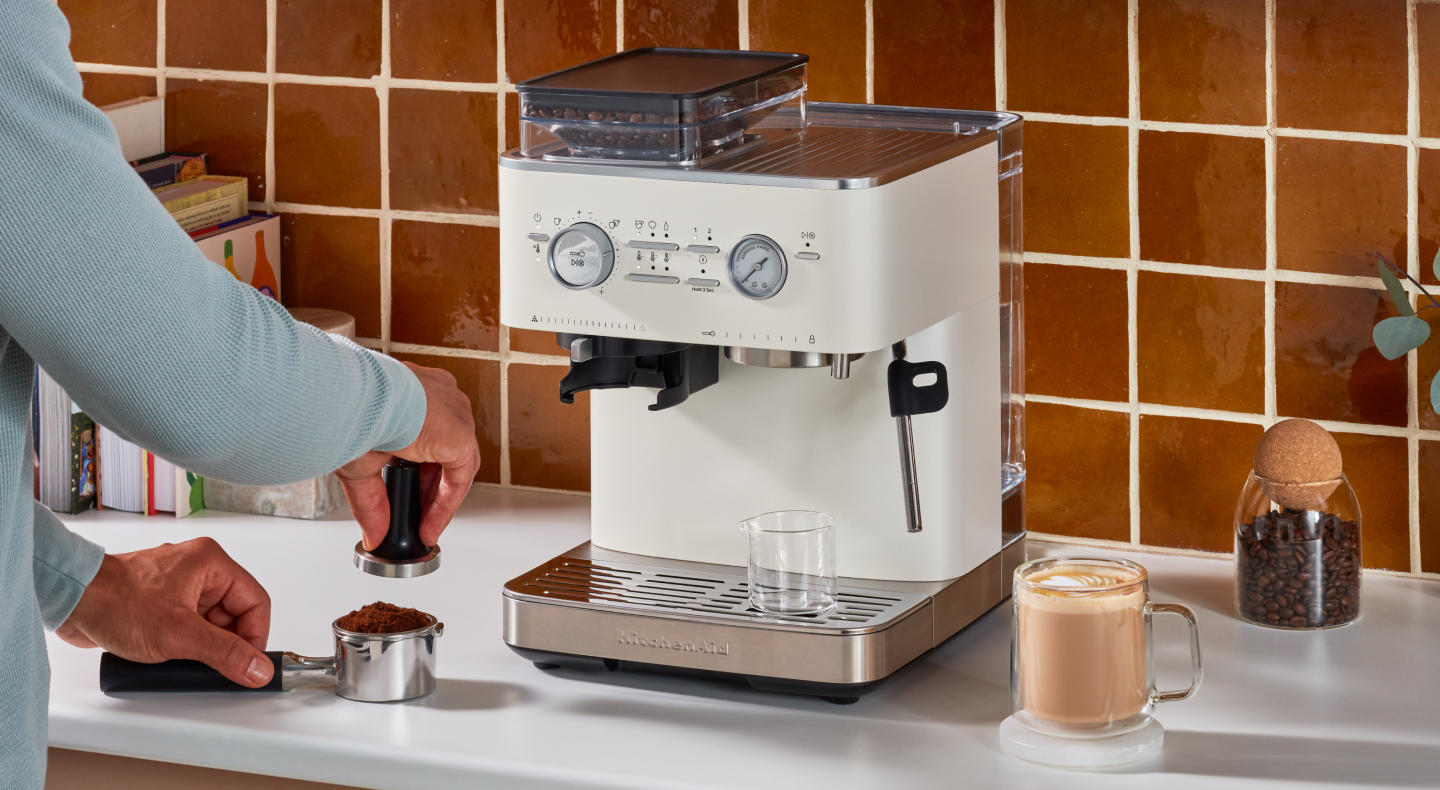 Person tamping espresso next to a KitchenAid® Semi Automatic Espresso Machine