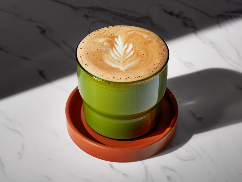 A piccolo latte in a green cup on a coaster