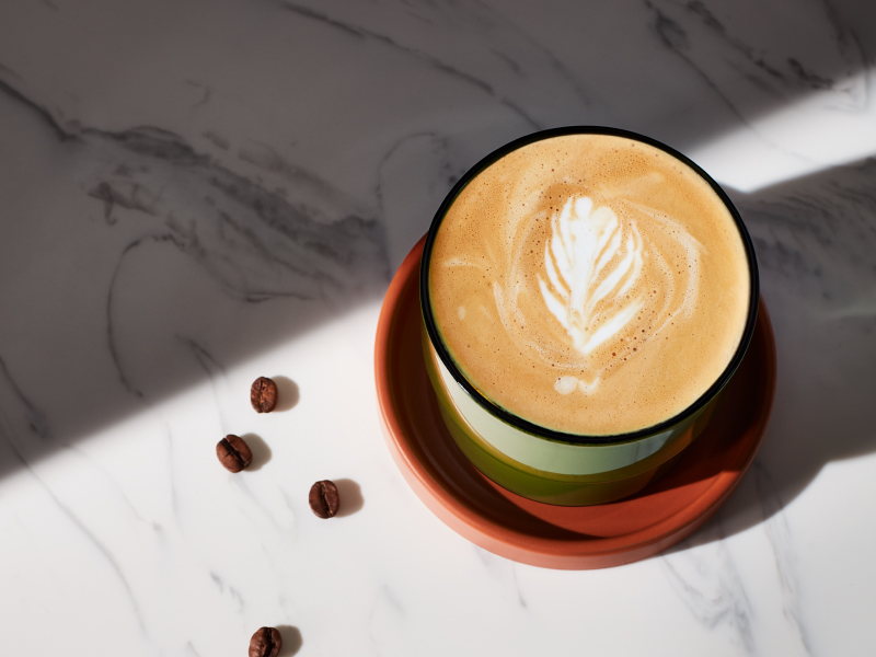 A flat white with foam art in a green cup on a granite countertop