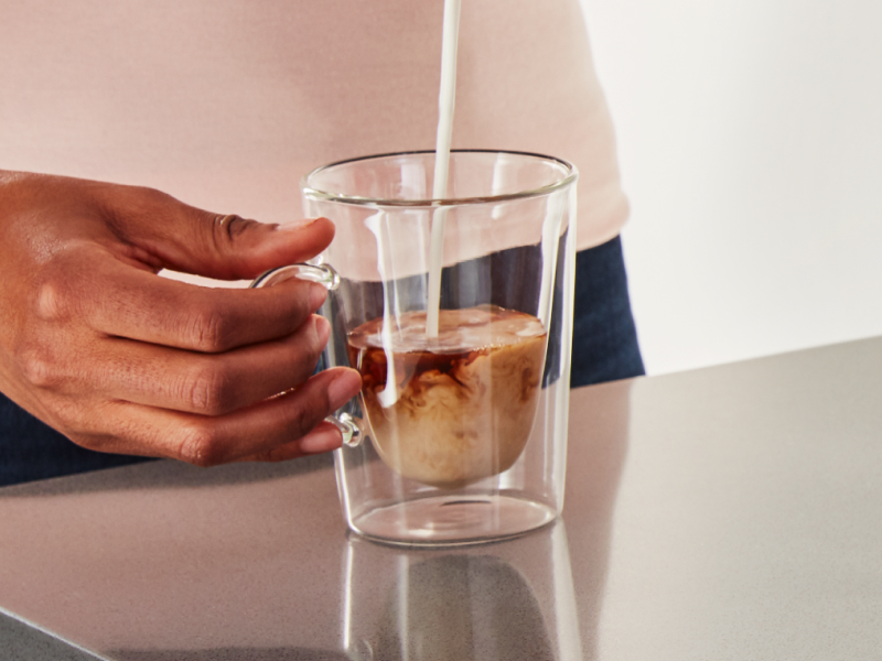 Person pouring steamed milk into a cortado in a glass mug