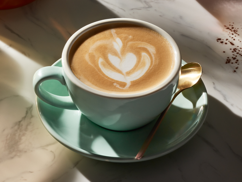 Latte with latte art in mint green tea cup on plate