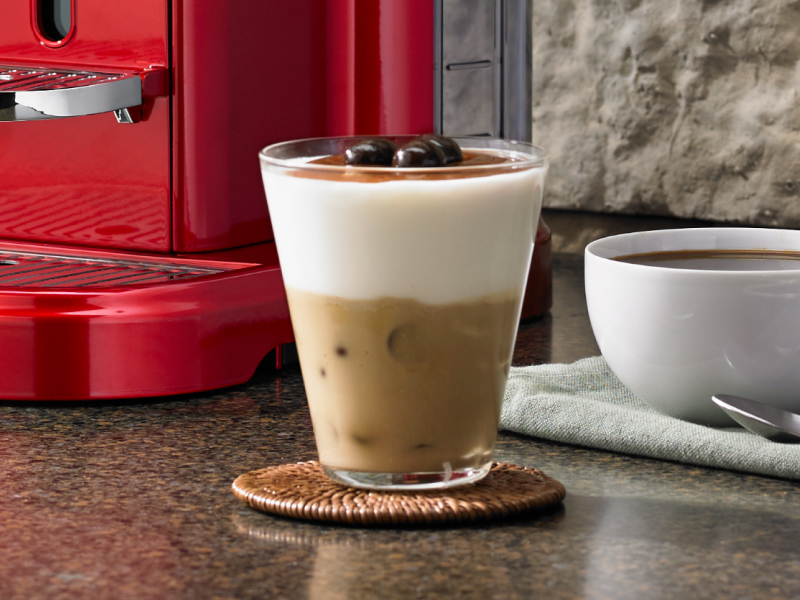 Latte macchiato on coaster near red espresso machine