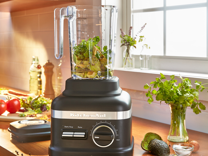 Pesto ingredients inside a black KitchenAid® blender