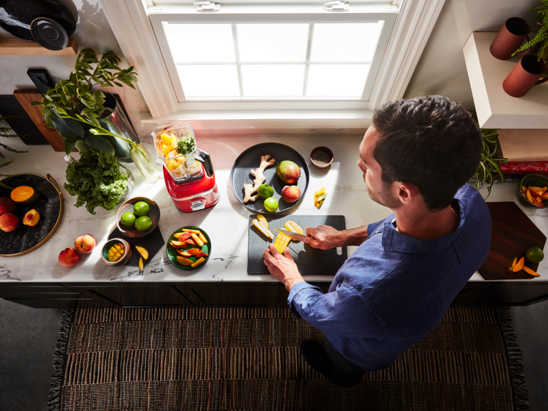 A person slicing fruit with a KitchenAid® blender nearby.
