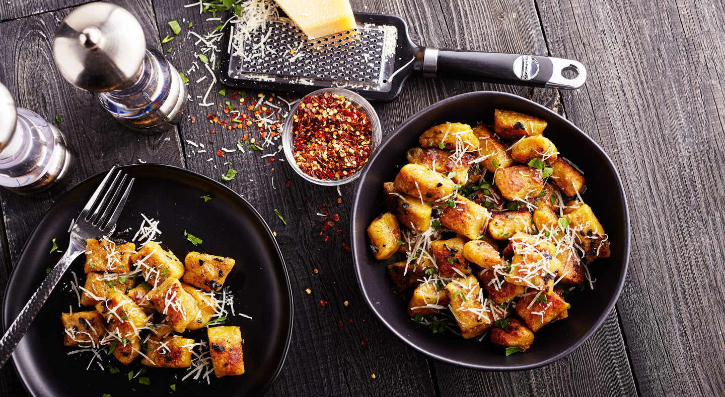 Two bowls of potato gnocchi meals with fresh parmesan, red pepper flakes and herbs.  Two bowls of potato gnocchi meals with fresh parmesan, red pepper flakes and herbs.