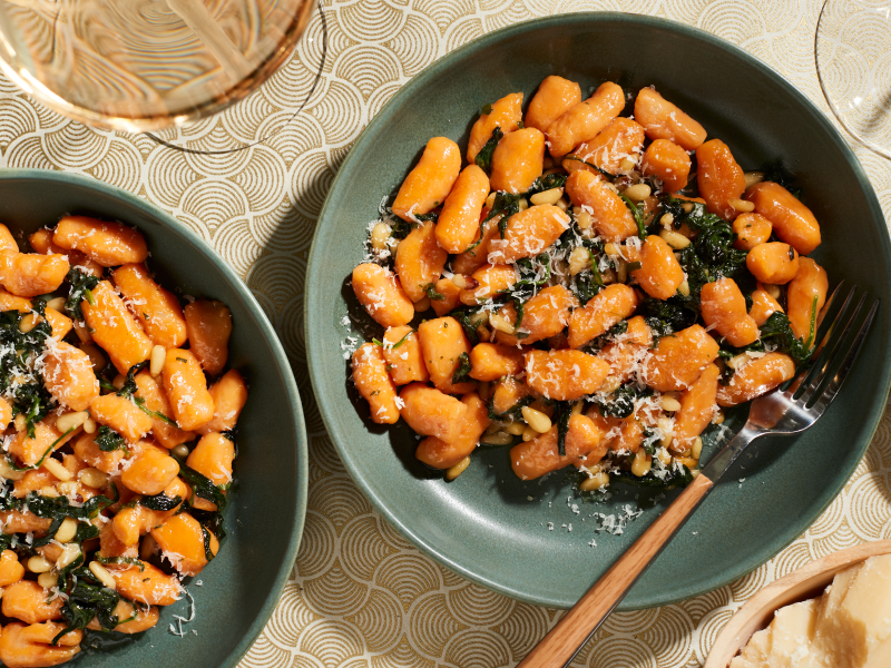 Two bowls of sweet potato gnocchi meals with shaved parmesan, spinach and herbs. Two bowls of sweet potato gnocchi meals with shaved parmesan, spinach and herbs.
