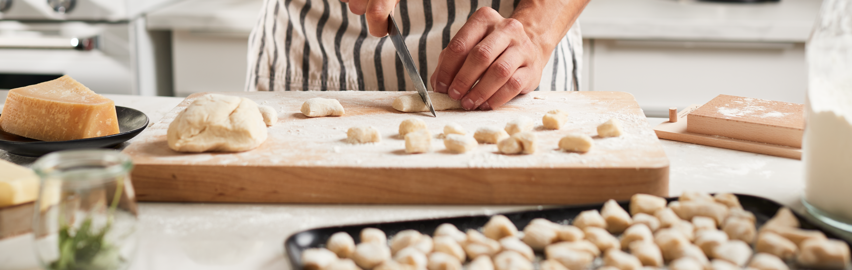 A man cutting pieces of potato gnocchi dough and placing them on a baking sheet in a modern kitchen.