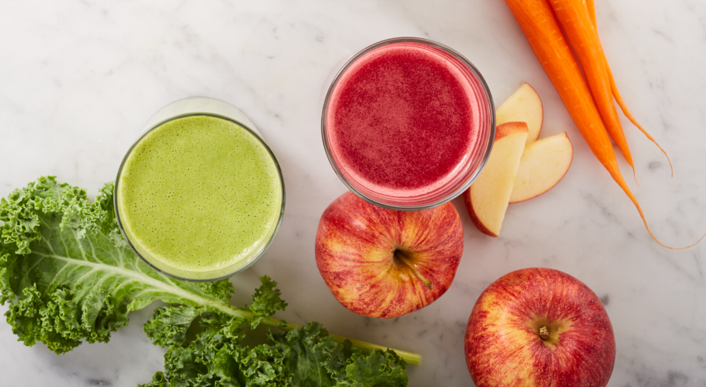 Green and red juices next to carrots, apples and lettuce on counter Green and red juices next to carrots, apples and lettuce on counter