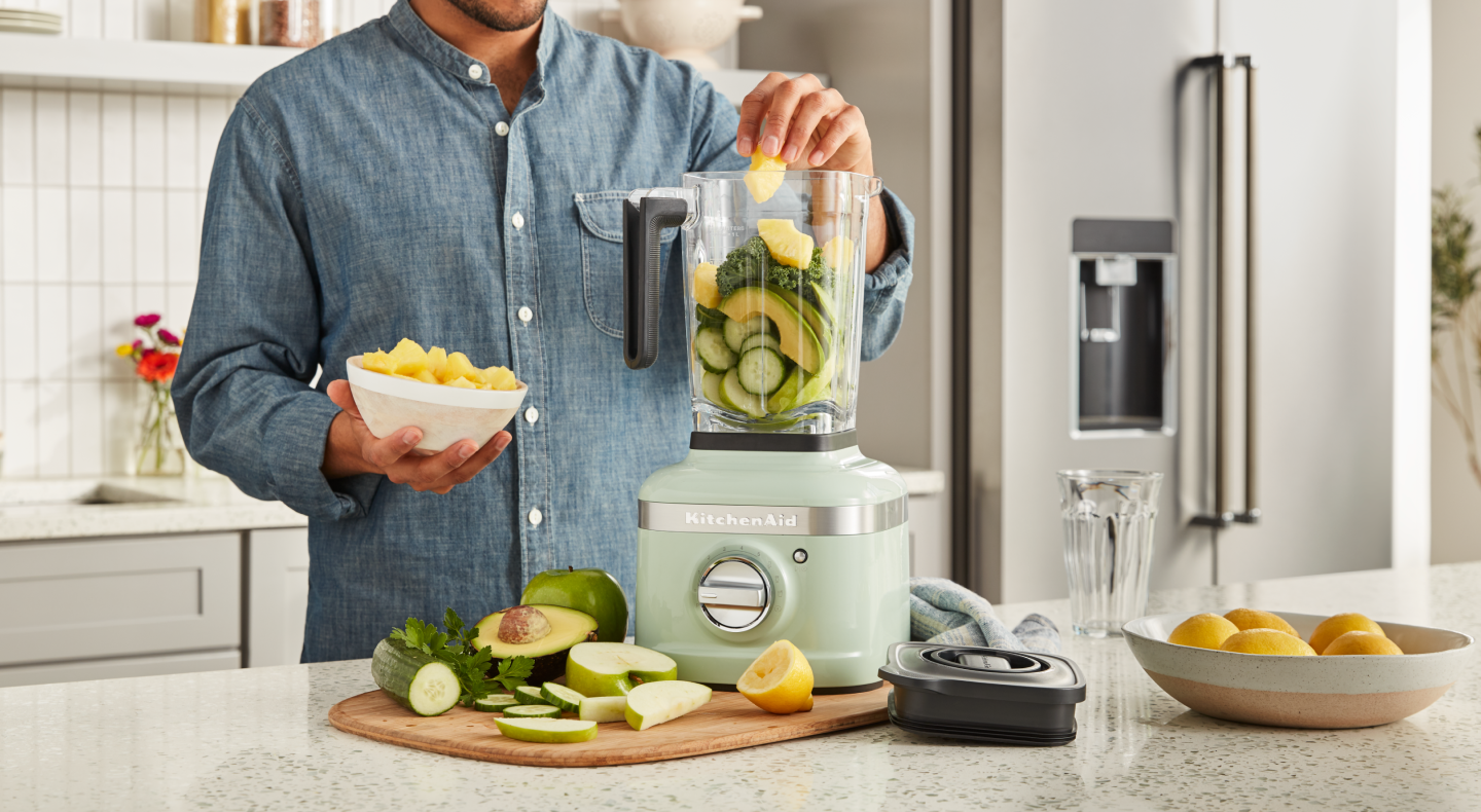 Person adding produce to a KitchenAid® blender Person adding produce to a KitchenAid® blender