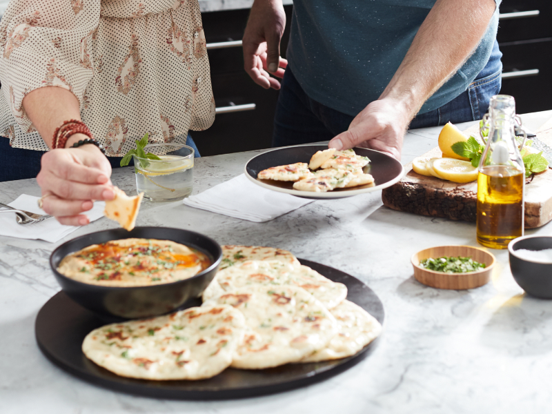 Person dipping pita bread into dish of baba ganoush next to whole pita pieces