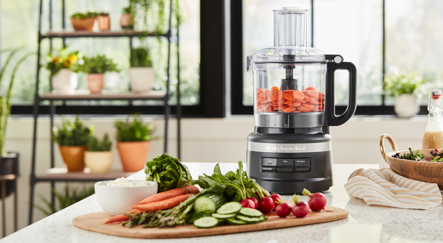 Cucumbers, carrots and radishes on cutting board next to food processor filled with sliced carrots Cucumbers, carrots and radishes on cutting board next to food processor filled with sliced carrots