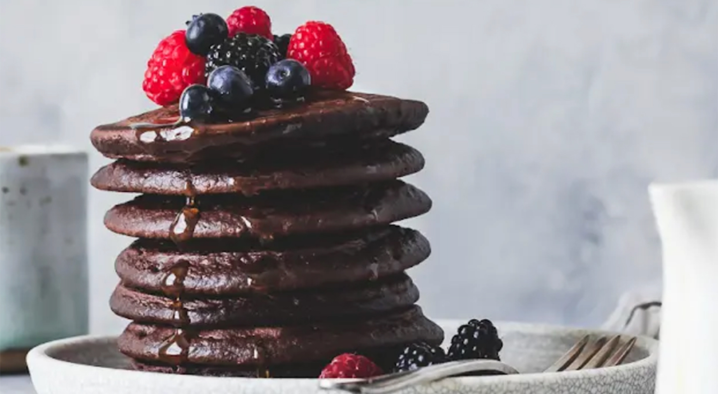 Stack of cocoa pancakes drizzled with syrup and topped with fresh fruit Stack of cocoa pancakes drizzled with syrup and topped with fresh fruit