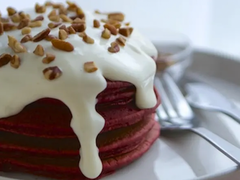 Stack of red velvet pancakes with cream cheese drizzle and nut topping Stack of red velvet pancakes with cream cheese drizzle and nut topping