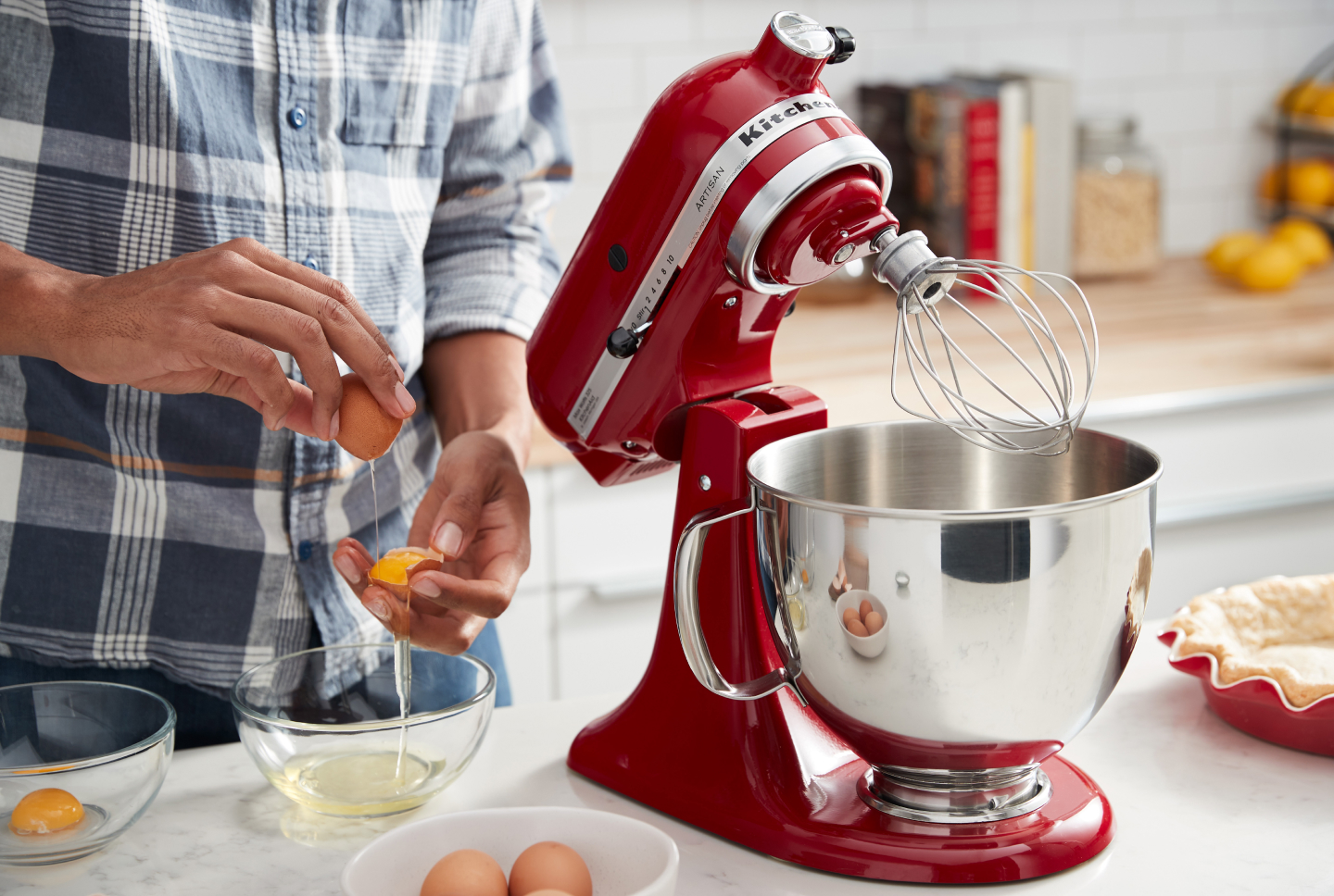 Person cracking eggs next to a KitchenAid® stand mixer with wire whip Person cracking eggs next to a KitchenAid® stand mixer with wire whip