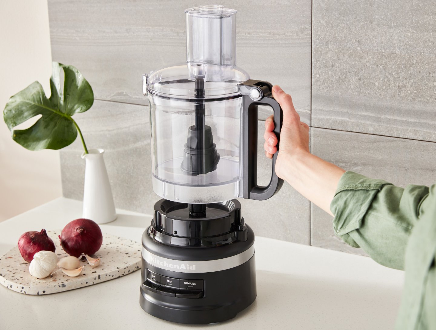 Person placing the work bowl of a black KitchenAid® food processor onto the base Person placing the work bowl of a black KitchenAid® food processor onto the base