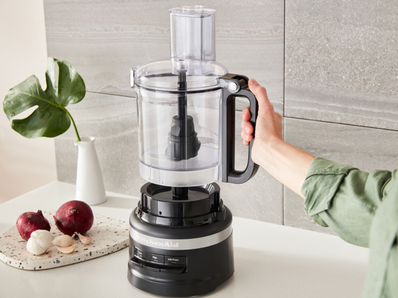 Person placing the work bowl of a black KitchenAid® food processor onto the base Person placing the work bowl of a black KitchenAid® food processor onto the base