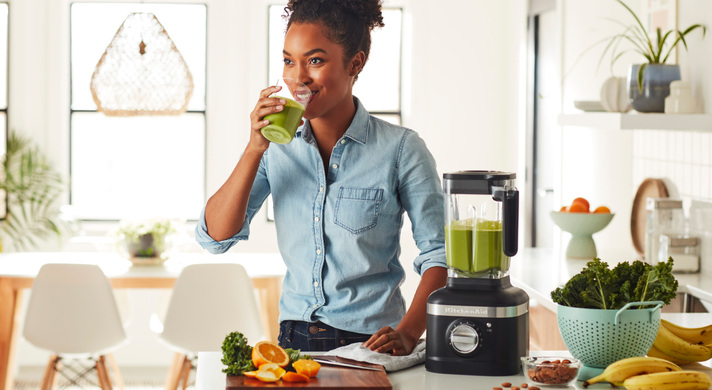 Person drinking a protein shake next to black KitchenAid® blender Person drinking a protein shake next to black KitchenAid® blender