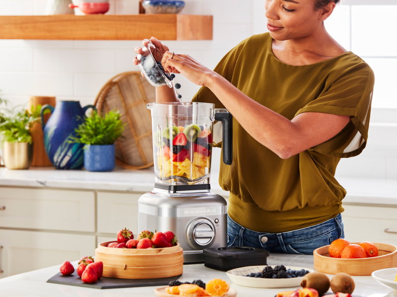 Person adding fruit to a KitchenAid® blender Person adding fruit to a KitchenAid® blender