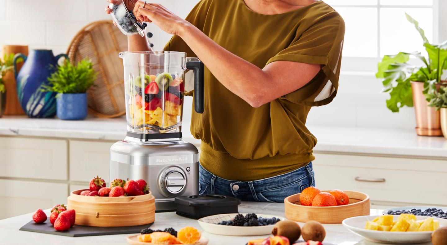 Person adding fruit to a KitchenAid® blender Person adding fruit to a KitchenAid® blender