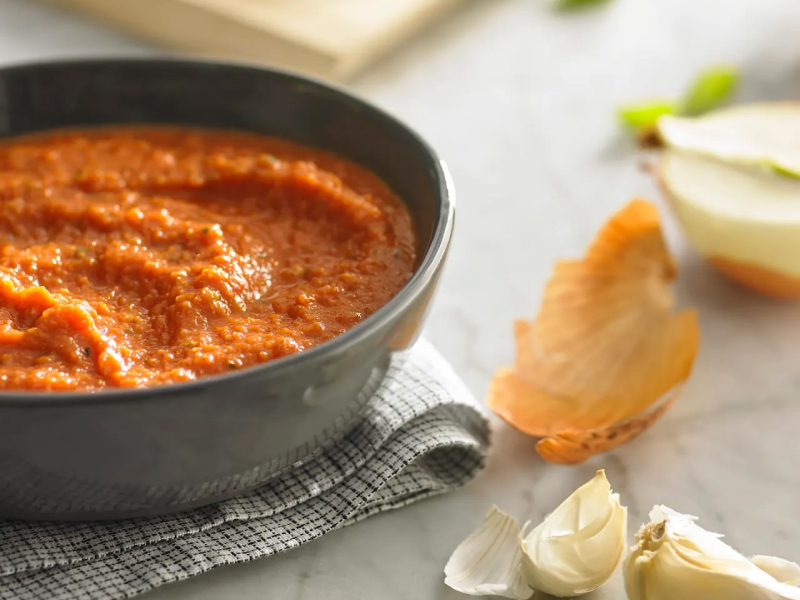 Bowl of marinara next to cloves of garlic