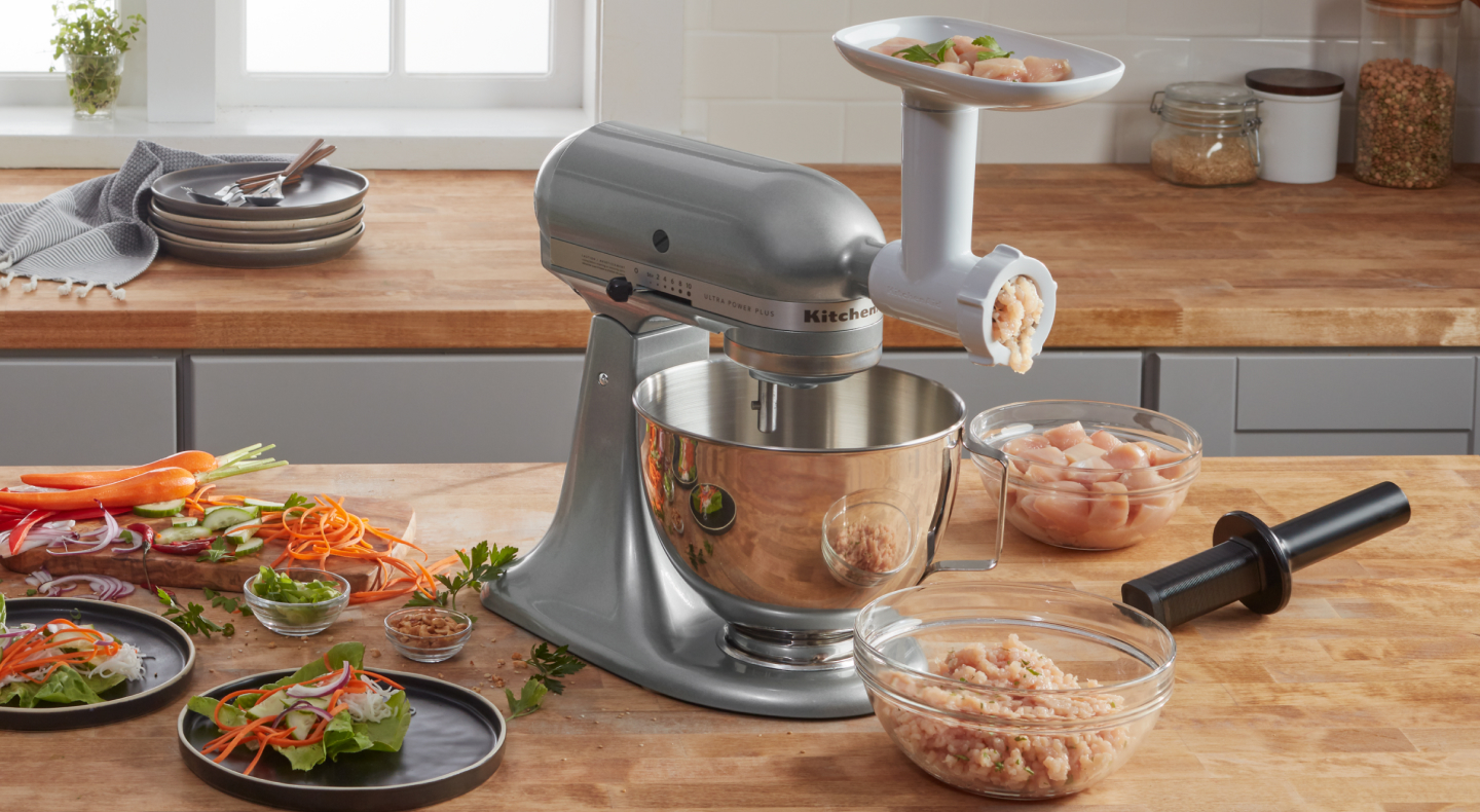 KitchenAid® stand mixer with KitchenAid® food grinder attachment and clear bowl of ground chicken KitchenAid® stand mixer with KitchenAid® food grinder attachment and clear bowl of ground chicken