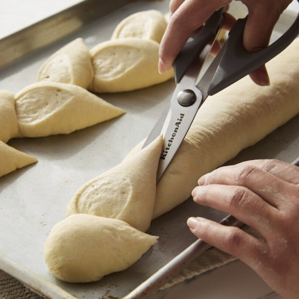 Person using kitchen scissors to score bread dough on a baking sheet