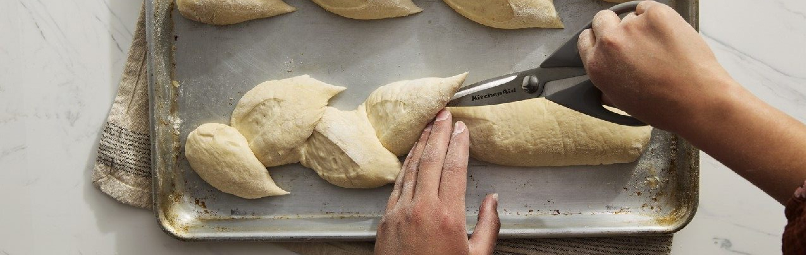 Person scoring bread on a baking sheet with kitchen scissors