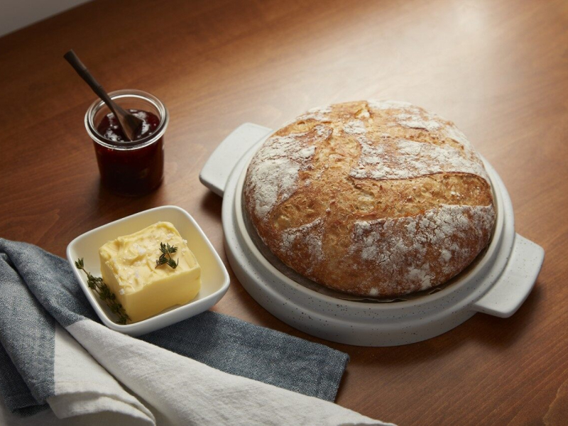 Round sourdough loaf next to a garnished butter dish and jar of jam spread