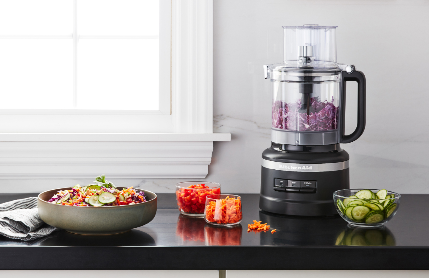 Shredded purple cabbage in a KitchenAid® food processor on a kitchen counter next to other shredded vegetables Shredded purple cabbage in a KitchenAid® food processor on a kitchen counter next to other shredded vegetables