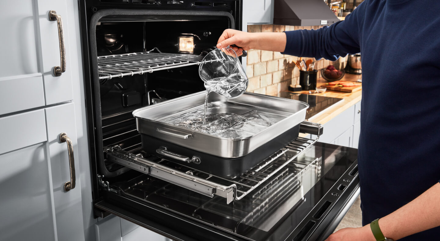 A person putting water in steaming cookware in the oven A person putting water in steaming cookware in the oven