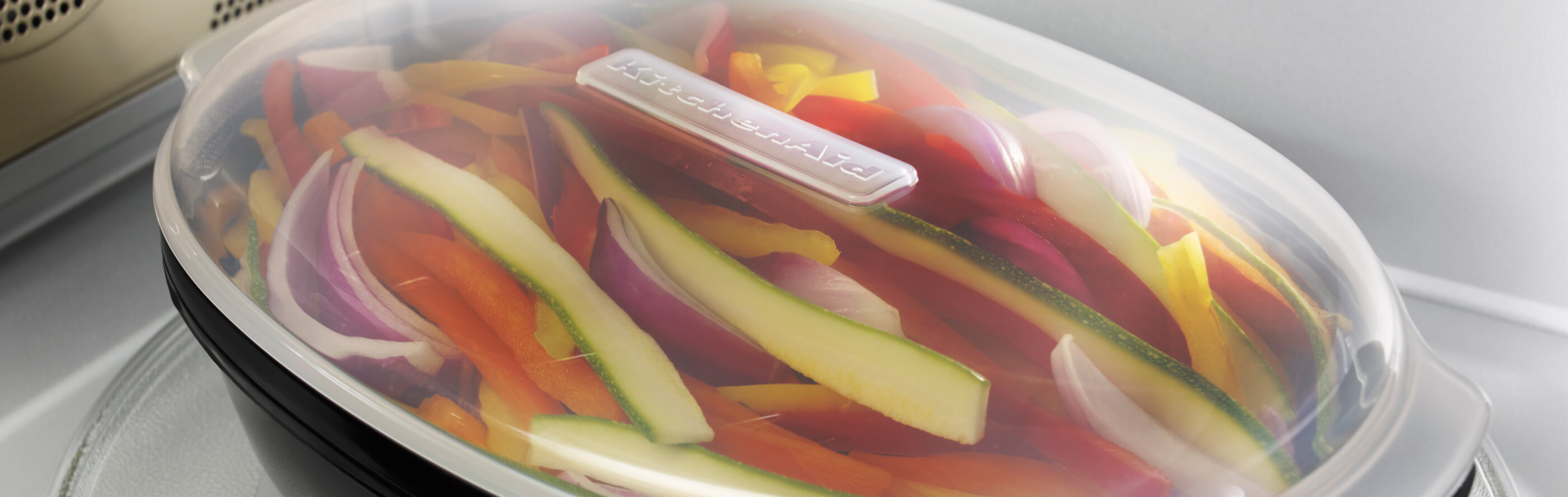 Sliced vegetables in a KitchenAid® steaming container in a microwave