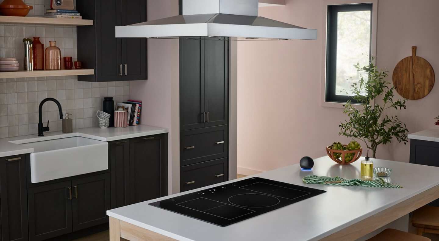 A neutral-toned kitchen with an induction cooktop set into an island with a sink and faucet in the background