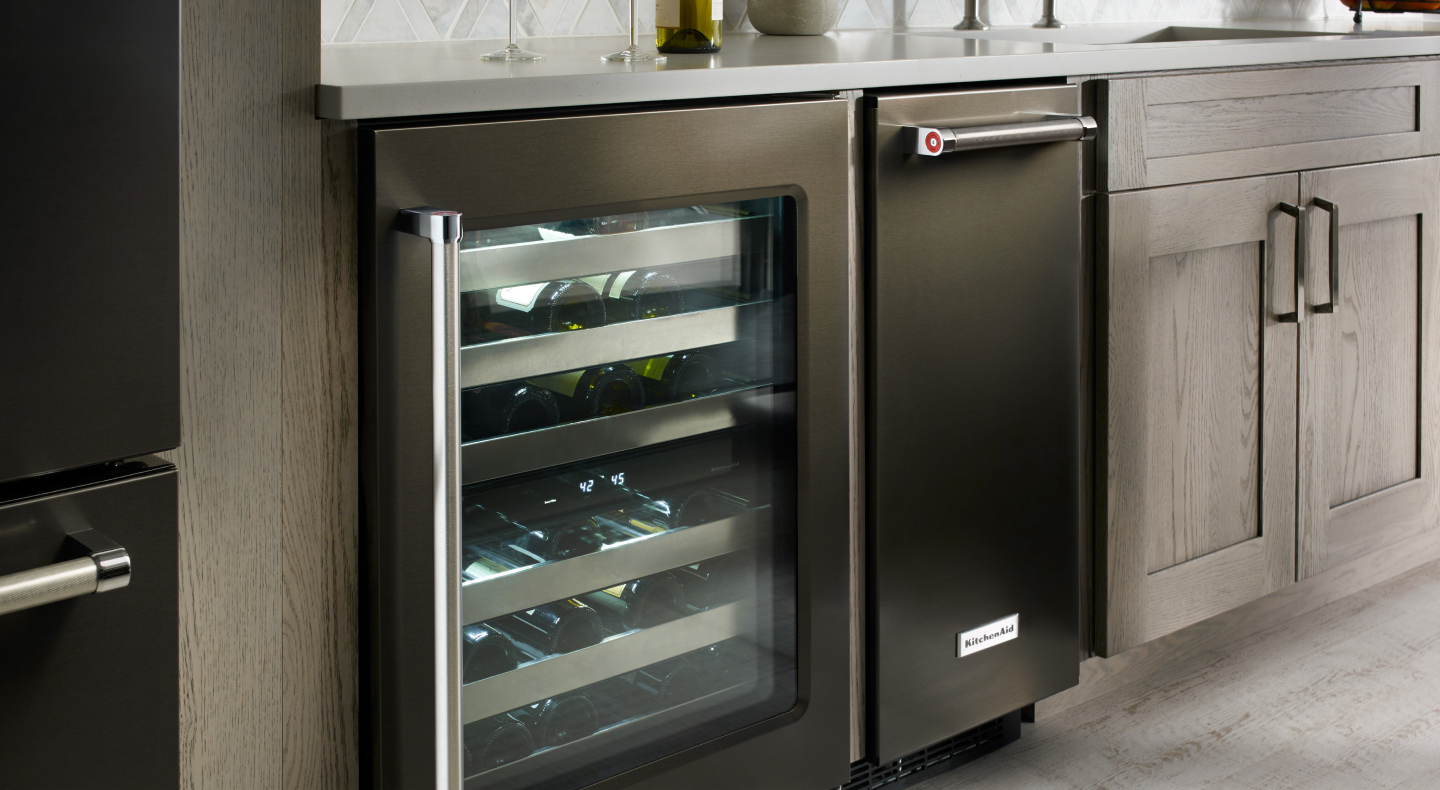 A black KitchenAid® ice maker next to an open wine cooler A black KitchenAid® ice maker next to an open wine cooler