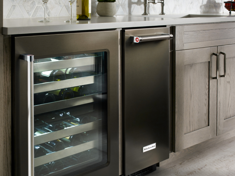 A black KitchenAid® ice maker next to an open wine cooler A black KitchenAid® ice maker next to an open wine cooler