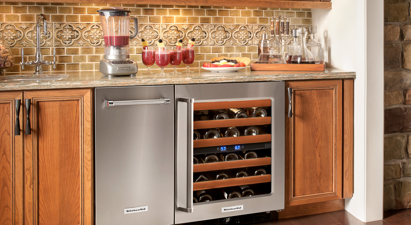 A black KitchenAid® ice maker next to an open wine cooler in a modern kitchen A black KitchenAid® ice maker next to an open wine cooler in a modern kitchen