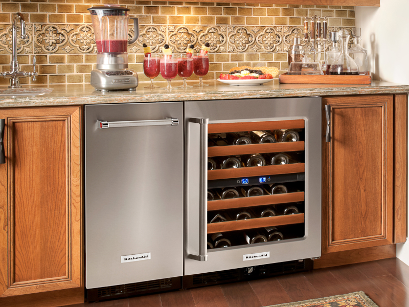 A black KitchenAid® ice maker next to an open wine cooler in a modern kitchen A black KitchenAid® ice maker next to an open wine cooler in a modern kitchen