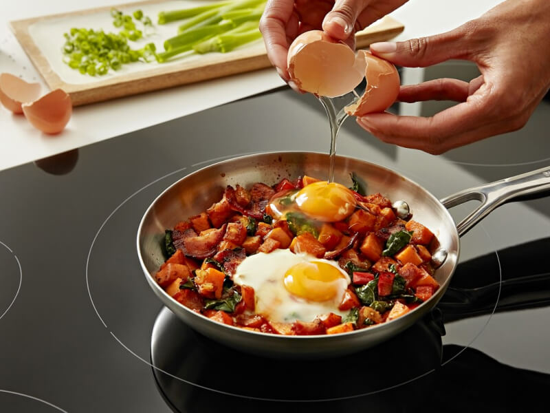 Person cracking an egg over a skillet of seared vegetables