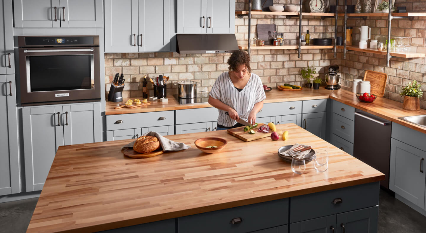 A woman chopping vegetables at a large, kitchen island