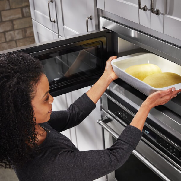 Person putting a 9-inch by 13-inch pan with bread dough in the microwave